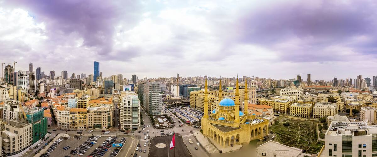 A cityscape with a prominent mosque featuring a blue dome, surrounded by modern and historical buildings.