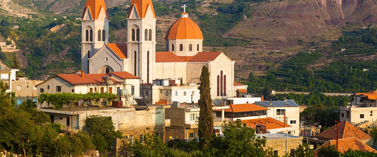 A church with two tall spires and a dome, surrounded by buildings and hills.