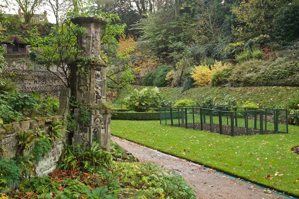 Un bâtiment historique en pierre, entouré d’une végétation luxuriante et d’un jardin bien entretenu.