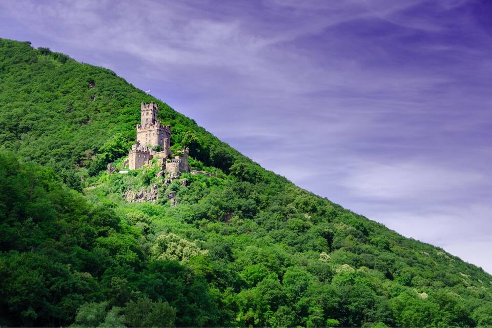 Eine Burg auf einem üppigen, grünen Hügel unter einem bewölkten Himmel.