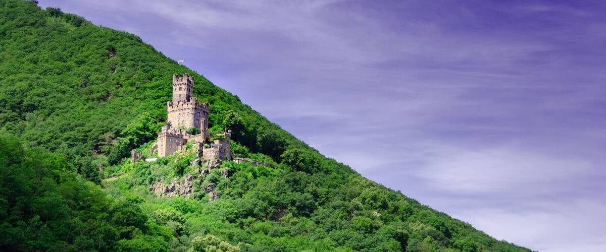A castle on a lush green hill under a cloudy sky.