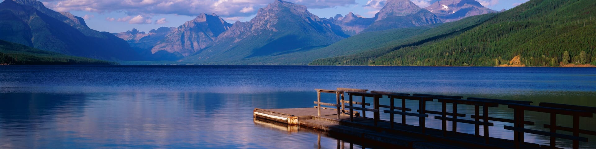 This is a boat dock at Lake McDonald. The blue water of the lake surrounds the dock with mountains in the background.
