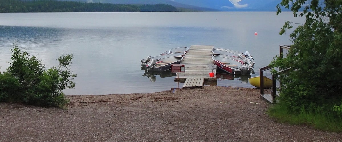 A lake with a dock and boats, surrounded by mountains and trees.
