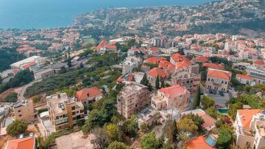 A coastal cityscape with red-roofed buildings, a prominent church, and a view of the sea.