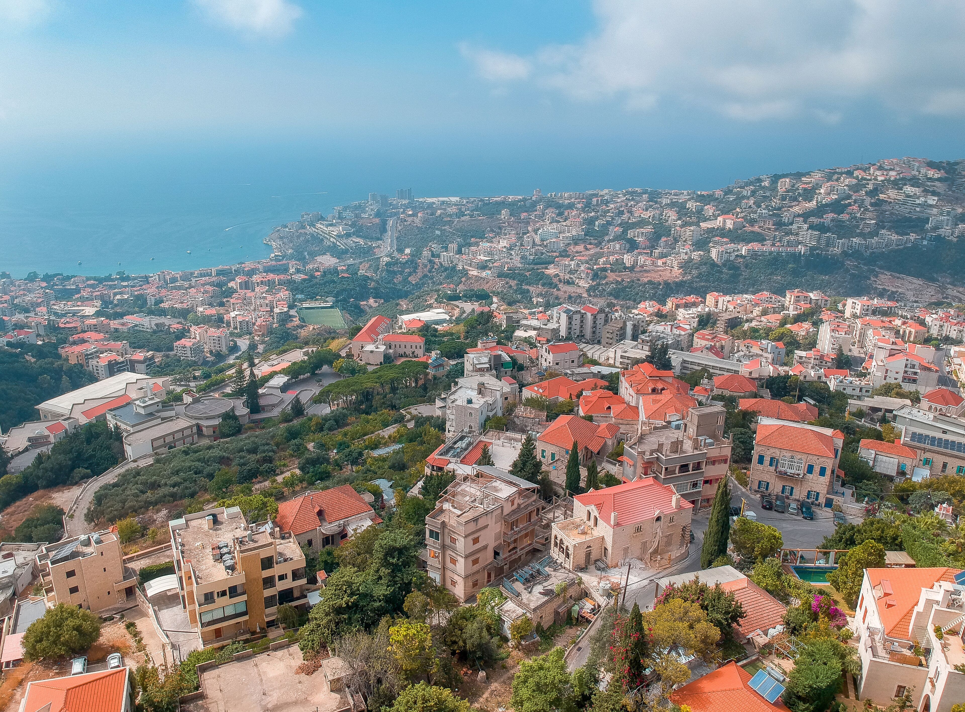 A coastal cityscape with red-roofed buildings, a prominent church, and a view of the sea.