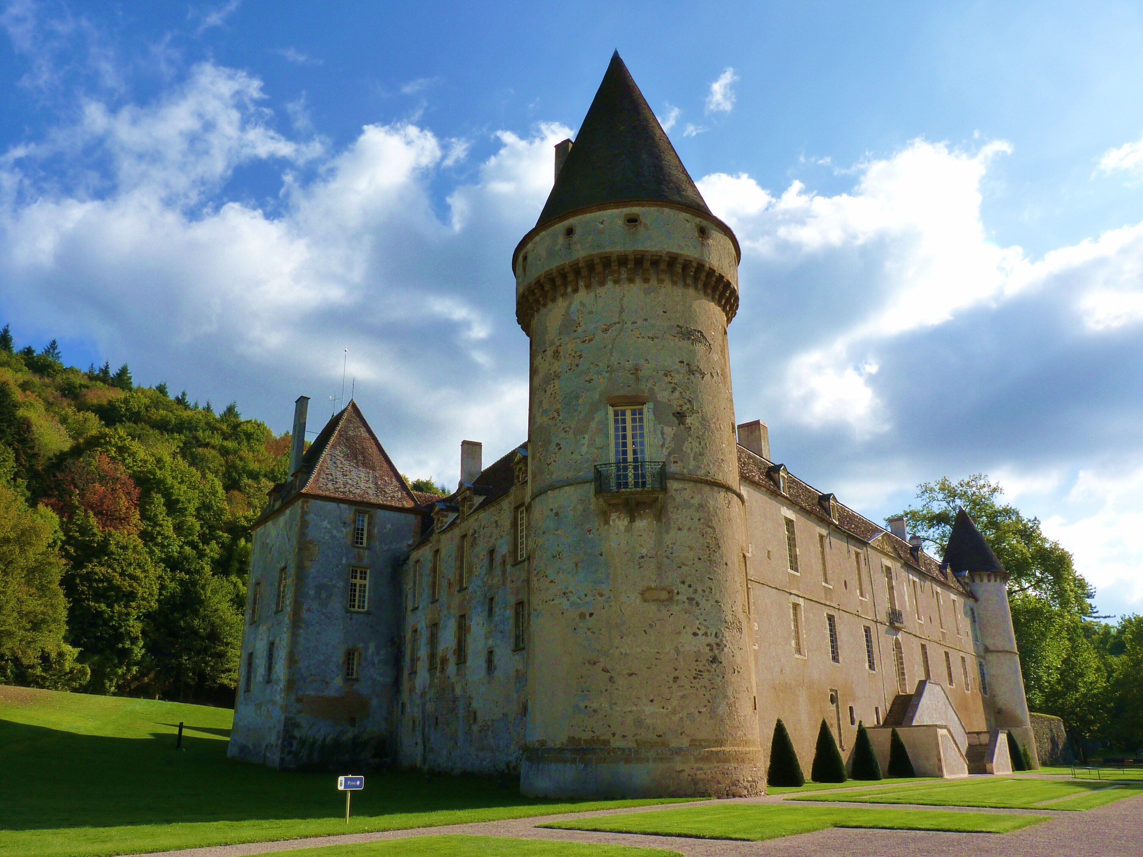 A historic castle with a prominent tower, surrounded by lush greenery and a clear sky.