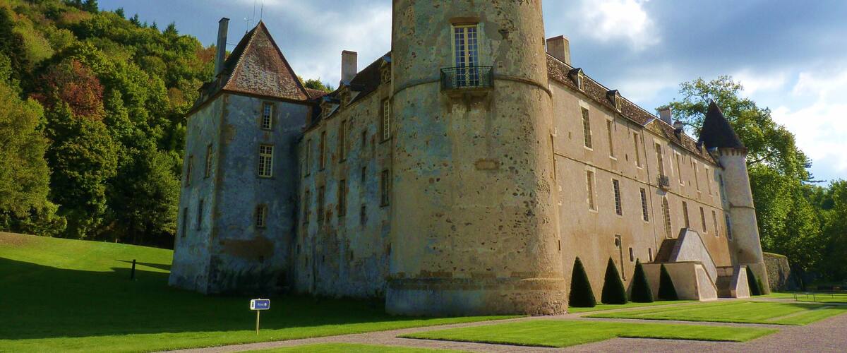 A historic castle with a prominent tower, surrounded by lush greenery and a clear sky.