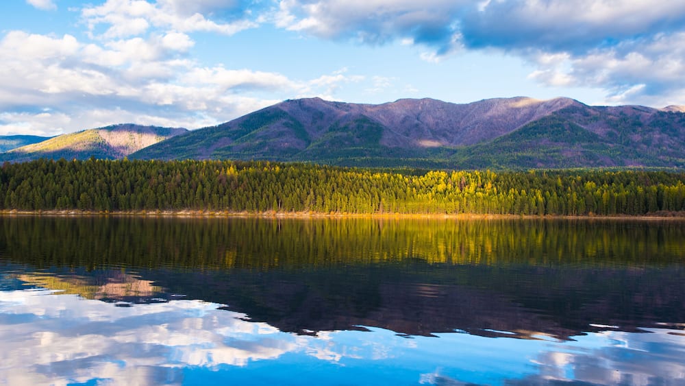 Un lac paisible oĂč se reflĂštent les montagnes et une forĂȘt dense.