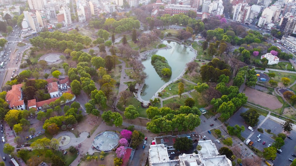An aerial view of a city park with a lake, surrounded by buildings and trees.