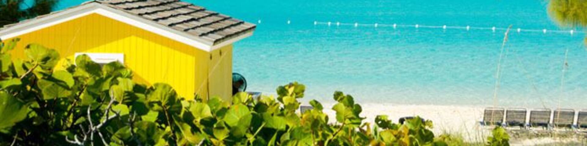 A colorful yellow beach cabana with the Holland America cruise ship Westerdam anchored off Half Moon Cay Bahamas