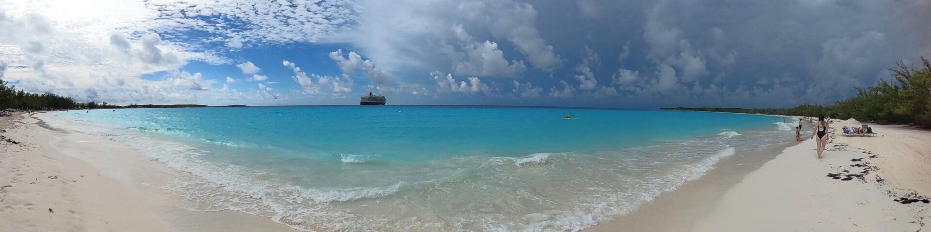 Uma praia com águas turquesa cristalinas, um cruzeiro ao longe e um céu parcialmente nublado.