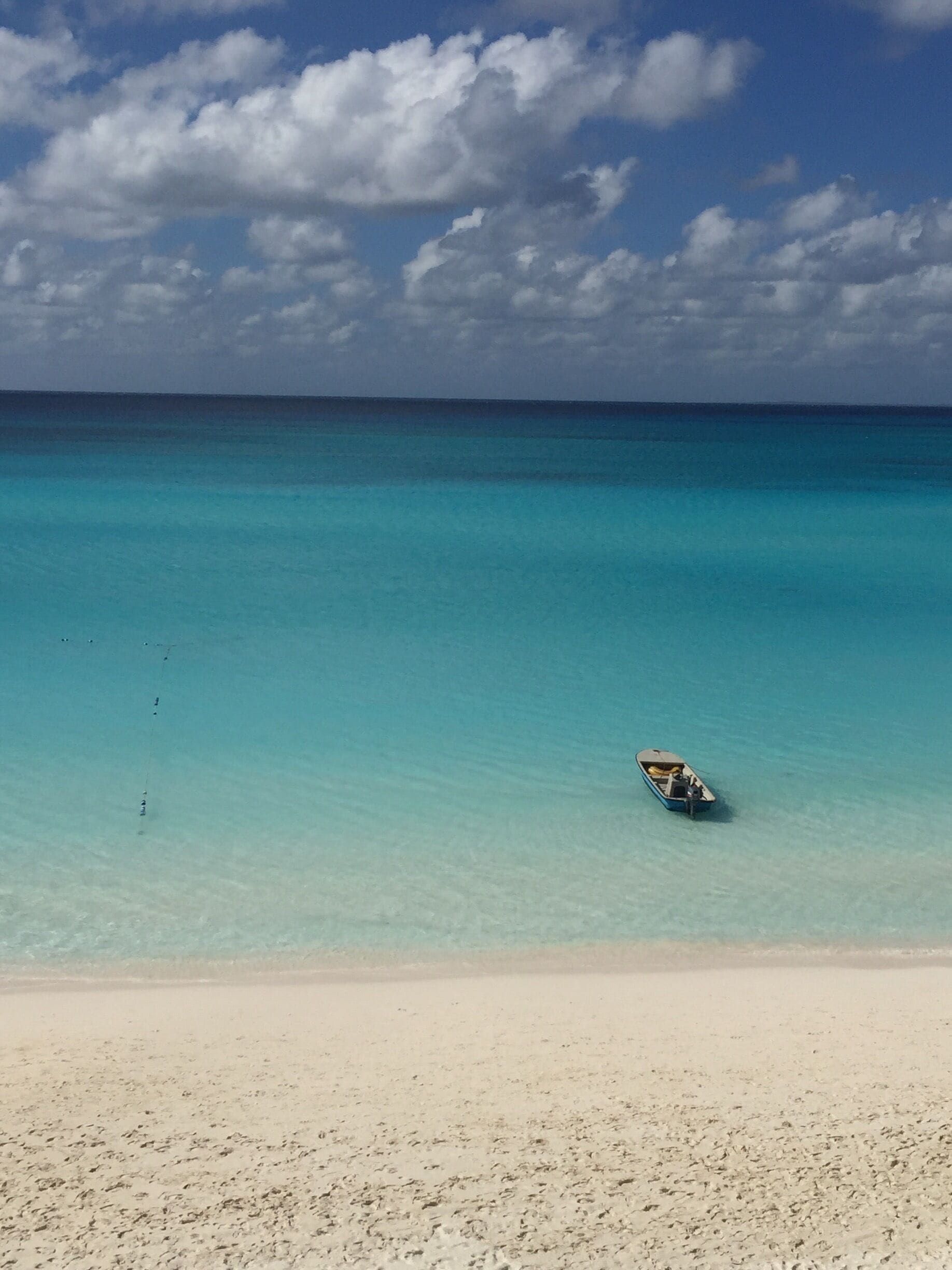A beach with clear turquoise water and a small boat on the shore.