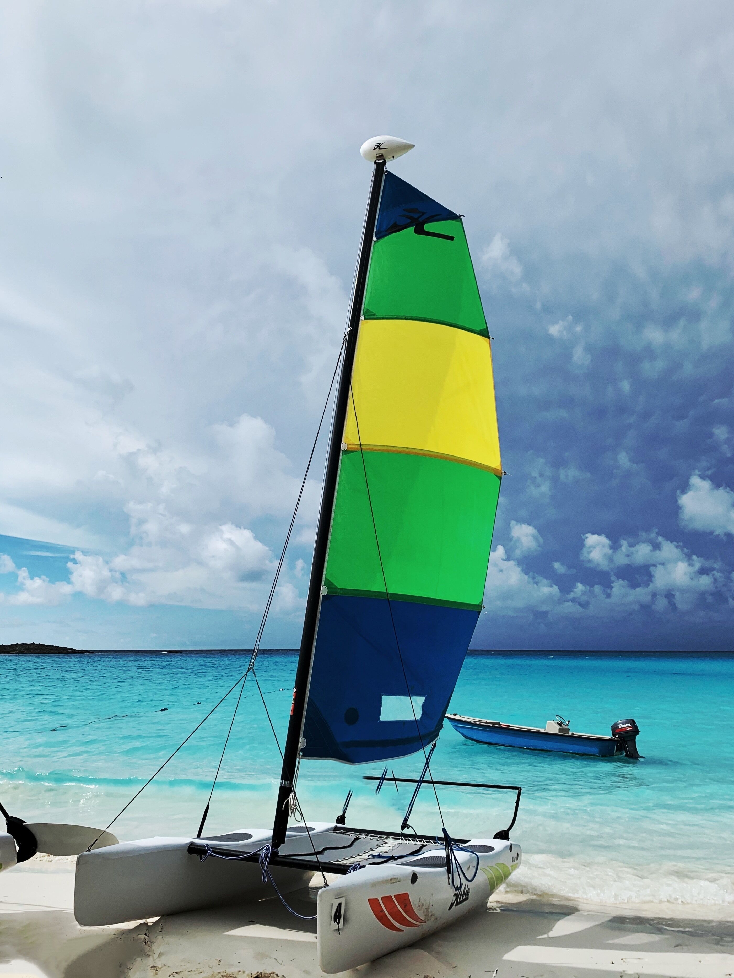 A sailboat with a multicolored sail on a beach.