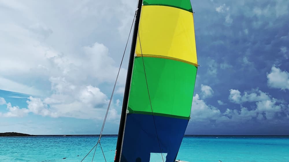 A sailboat with a multicolored sail on a beach.