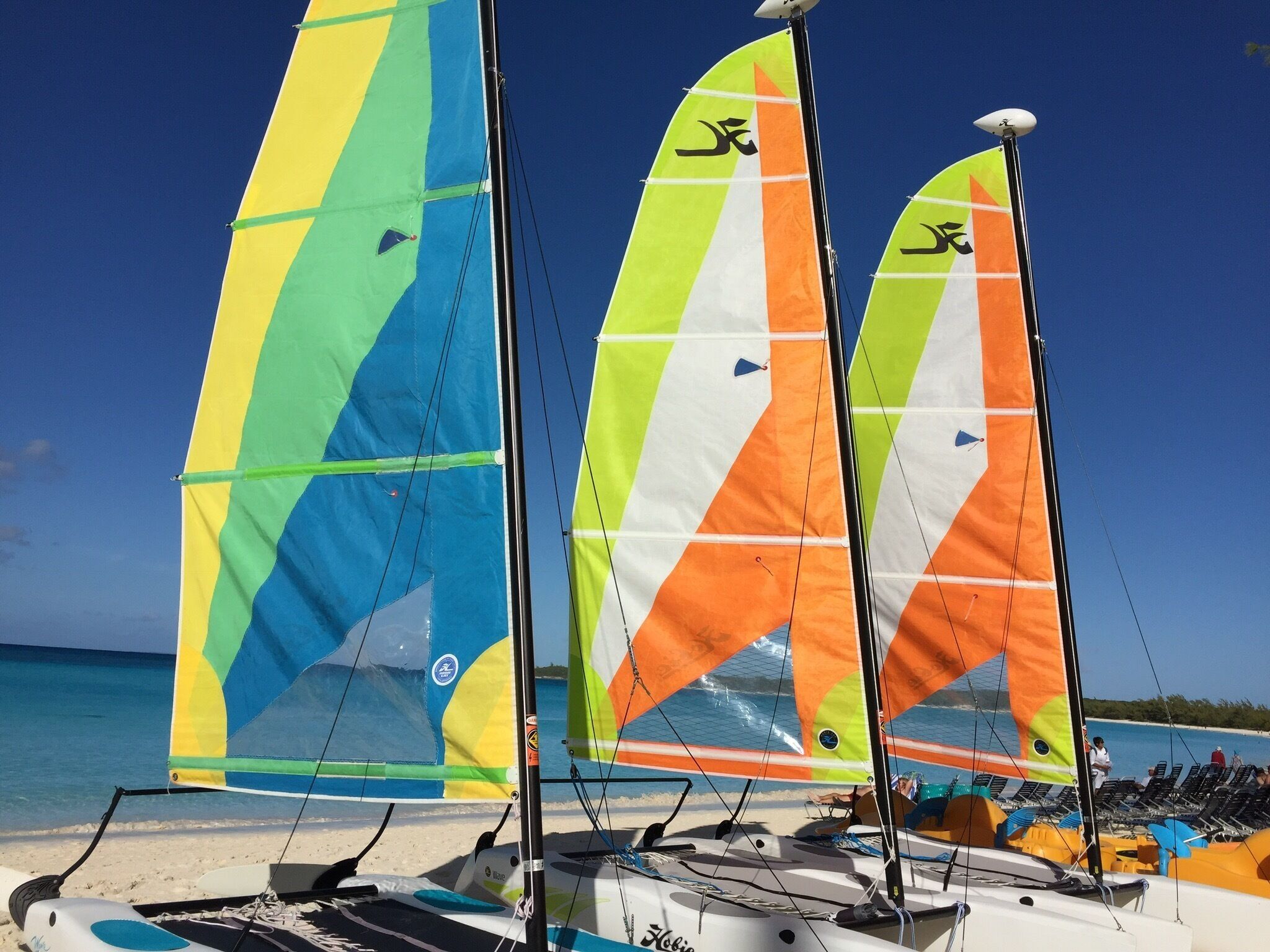 Three colorful sailboats on a beach with clear blue water.