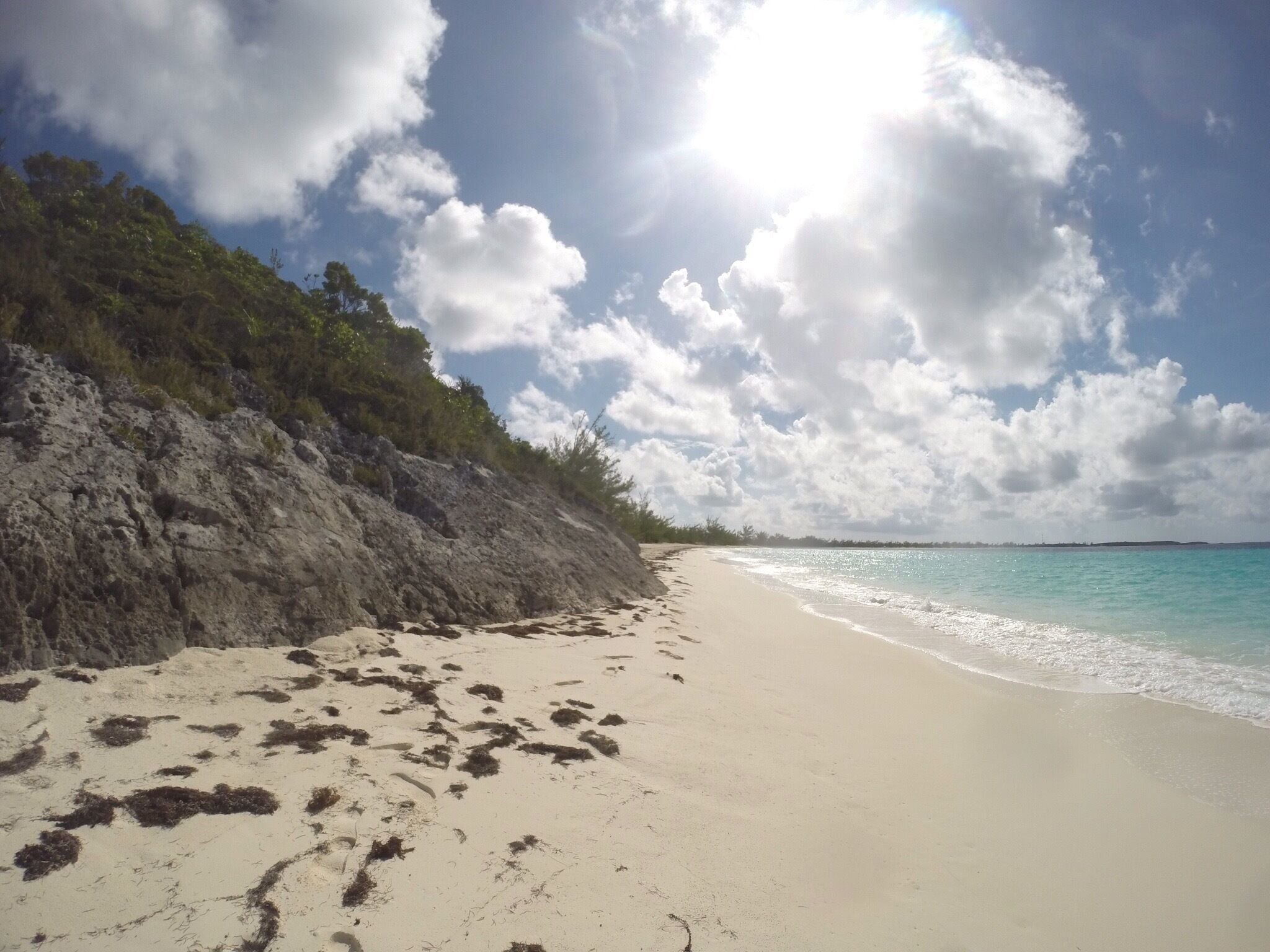 A beach with clear turquoise water, a sandy shore, and a rocky cliff with vegetation.
