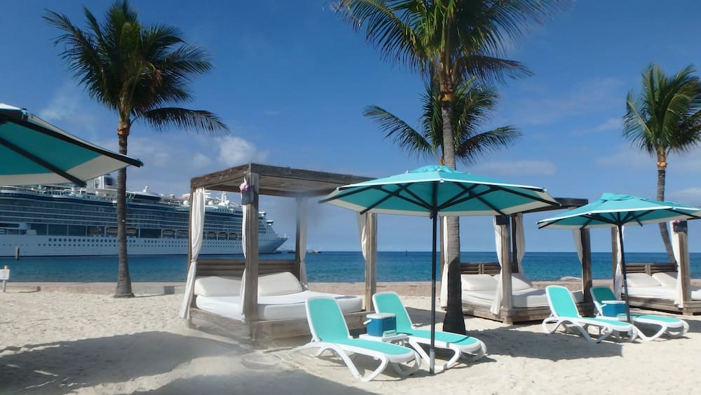 Sunshades and Beach beds on the white sand in Coco Cay, Bahamas and cruise ship in background