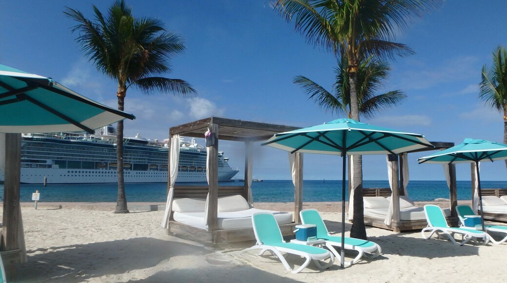 Sunshades and Beach beds on the white sand in Coco Cay, Bahamas and cruise ship in background