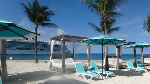 Sunshades and Beach beds on the white sand in Coco Cay, Bahamas and cruise ship in background