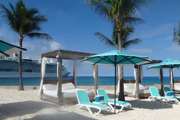 Sunshades and Beach beds on the white sand in Coco Cay, Bahamas and cruise ship in background