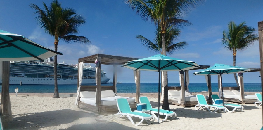 Sunshades and Beach beds on the white sand in Coco Cay, Bahamas and cruise ship in background