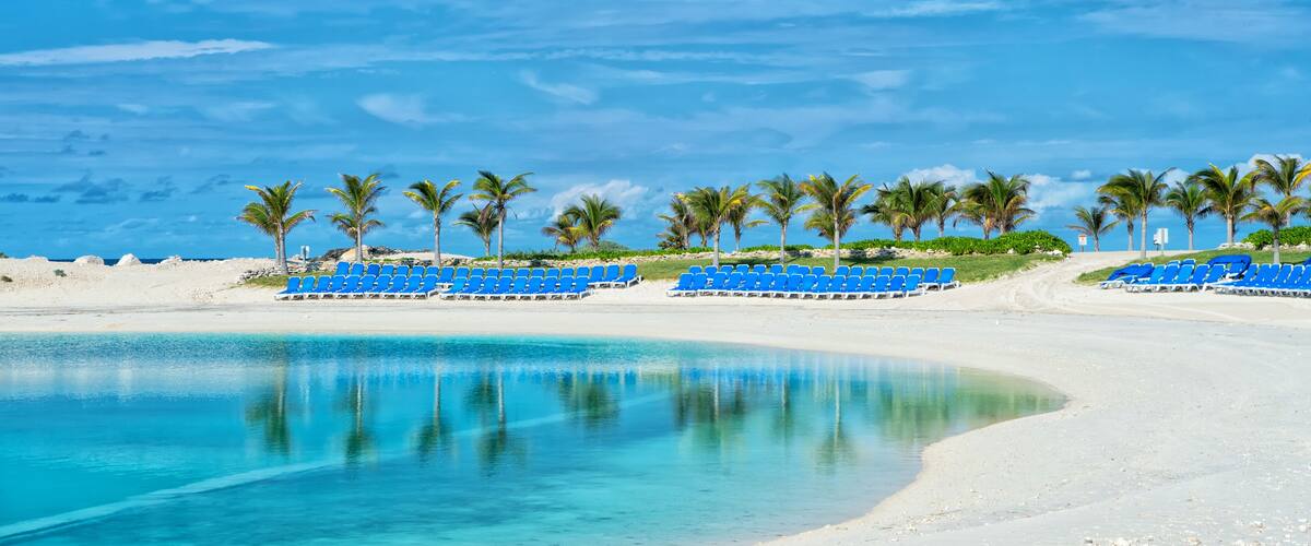 A beach with clear turquoise water, white sand, and rows of blue chairs.