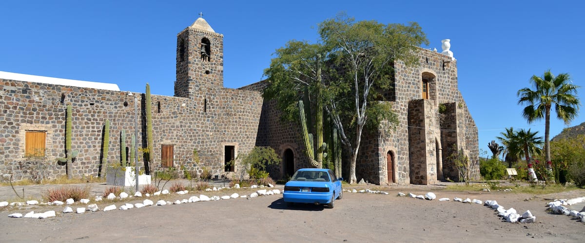 A historic stone building with a bell tower and a blue car parked in front.
