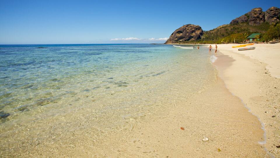 A clear beach with shallow water, a rocky outcrop, and a few people.