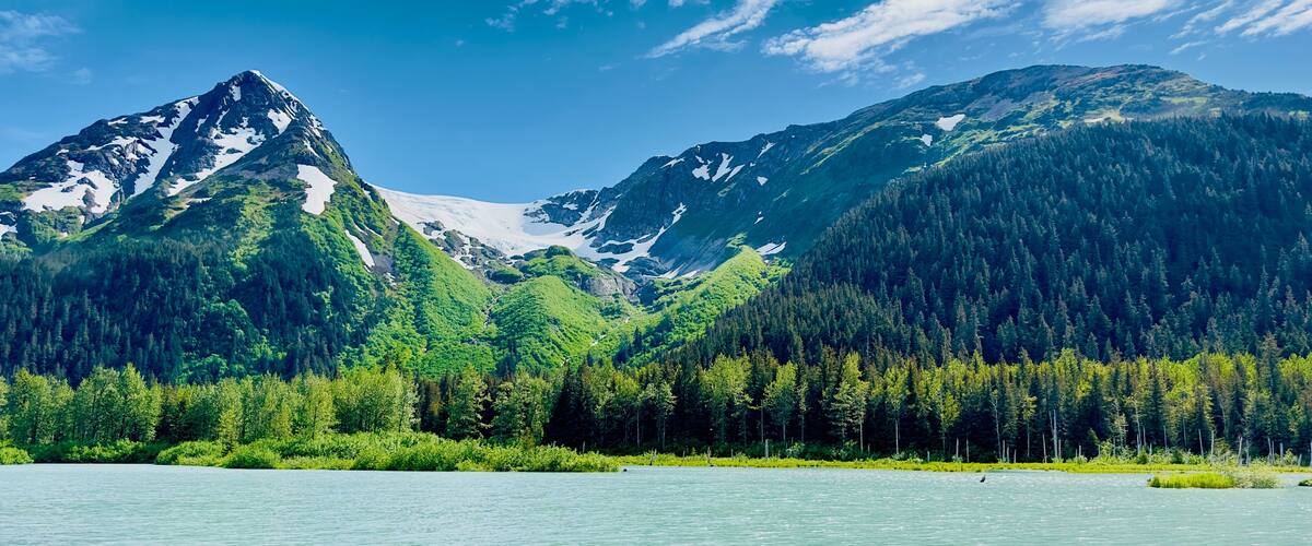 Eternal snow on Girdwood Glacier in Alaska USA under clear blue Sky and in front a grey blue lake - landscape shot taken on the water from a boat: concept of summertime, travel, outdoor