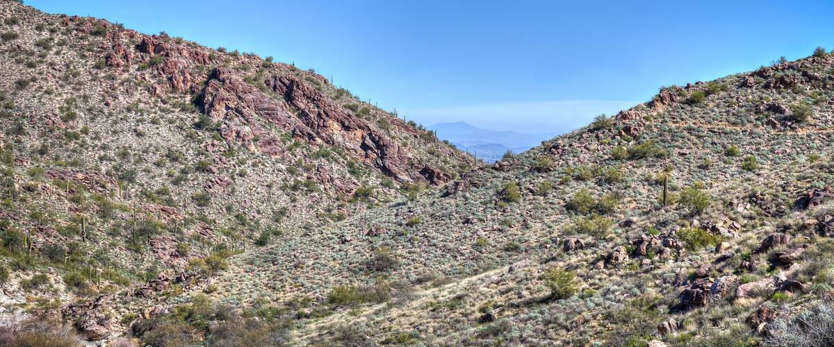 A rugged desert landscape with rocky hills and sparse vegetation under a clear blue sky.
