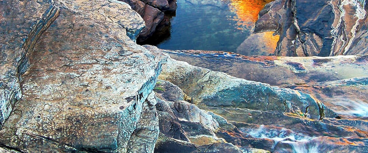 We returned to the motorhome for lunch and moved on to Knox Gorge, some 20 kilometres away. This too was special and I learned that it actually links up with where we were earlier in the day and you can do an 8 hour trek from here and come up the ladder at Hancock Gorge. That would be one heck of a day!
The light wasn’t right at Knox though so we moved around to nearby Joffre Falls where it was better, though it was just on sunset so there wasn’t much time left. The evening hues were the like of which I’d never seen before. Strange ochres beguiled the eye and the reflections of sunset kissed canyon tops in the water below had an air of magic about them. The whole scene was surreal and true all at the same time.
The splashing of the water down the steps of the cascade just added to the allure as I watched it then move through crystalline pools shaded by the erratic cliffs whose ancient layers would dazzle red in the noonday sun.
Everything about it could be explained except the overwhelming feeling that this place was something special and I wouldn’t see its like again.
#Nature