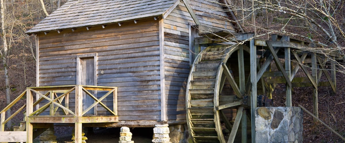 A wooden mill with a water wheel and a wooden staircase leading up to it.