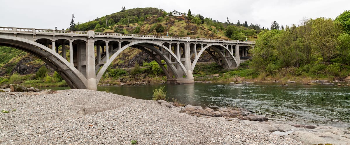 A stone bridge over a river with a hill in the background.