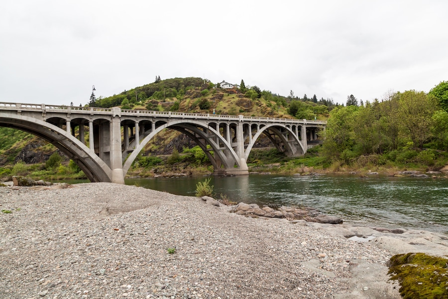 A stone bridge over a river with a hill in the background.