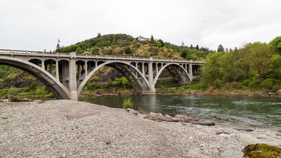 A stone bridge over a river with a hill in the background.