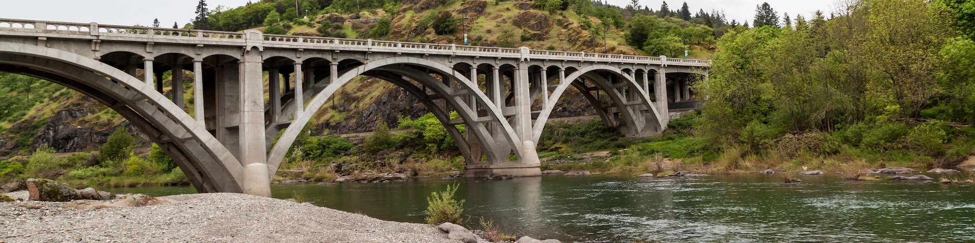 Uma ponte de pedra sobre um rio, com uma colina ao fundo.