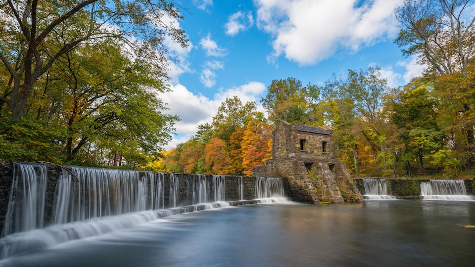 A waterfall cascading over a stone structure surrounded by autumn foliage.