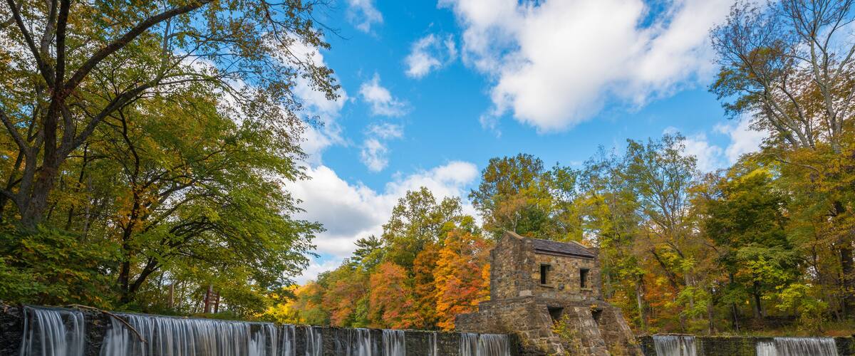 A waterfall cascading over a stone structure surrounded by autumn foliage.
