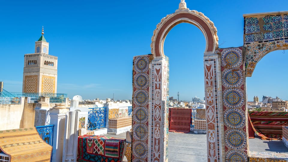 Un toit-terrasse agrémenté d’arcs décoratifs et, au loin, un minaret.