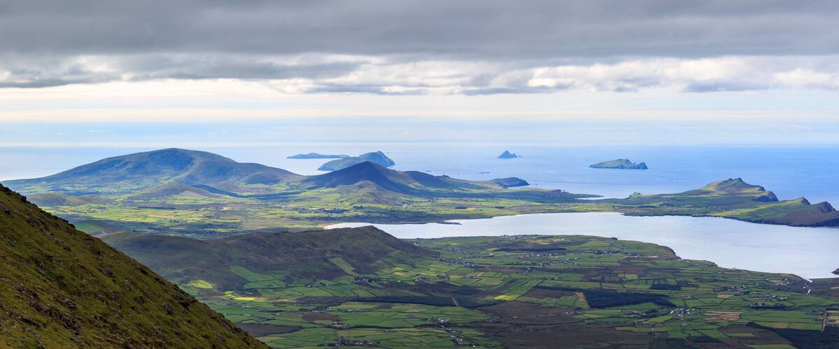 A coastal landscape with green fields, a lake, and distant islands under a cloudy sky.