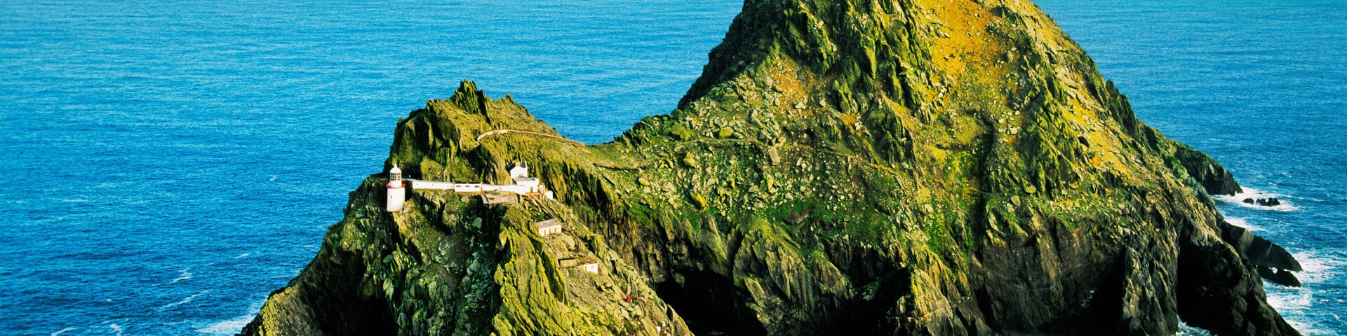 A rugged, green island with a lighthouse and a winding road.