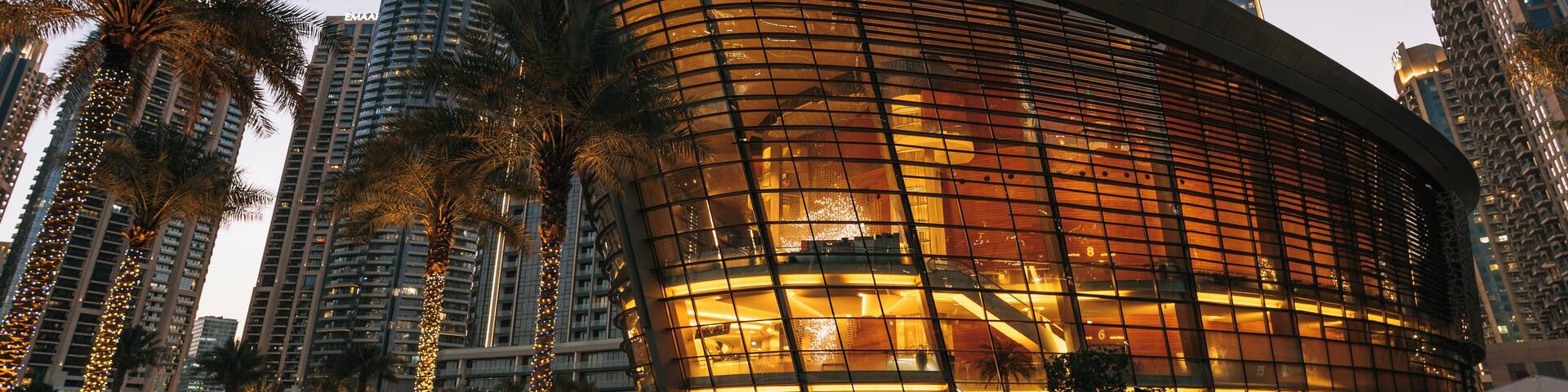 A modern building with a curved facade, palm trees, and high-rise buildings in the background.