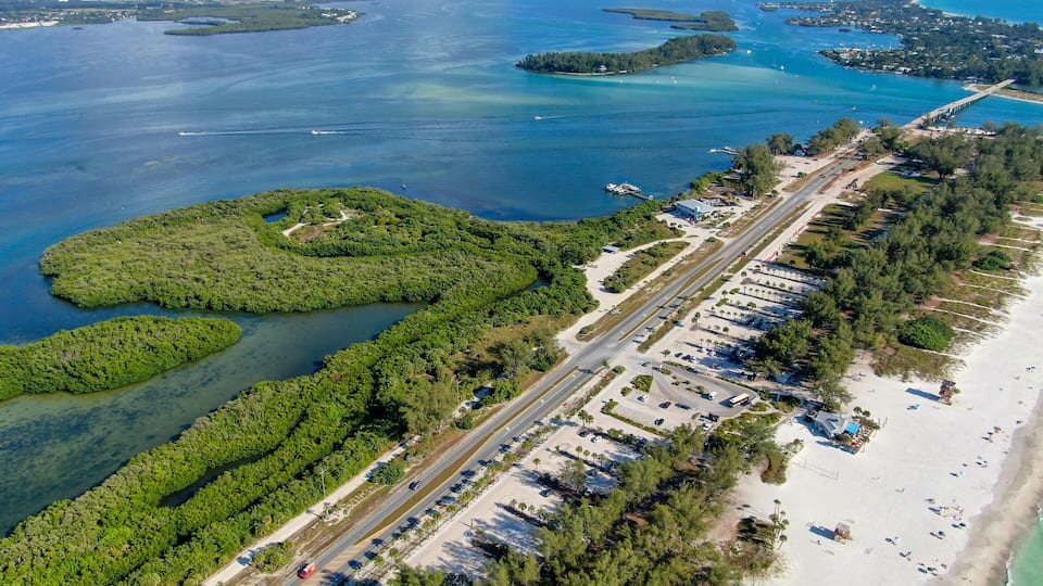 An aerial view of a coastal area with a beach, parking lot, and a road.