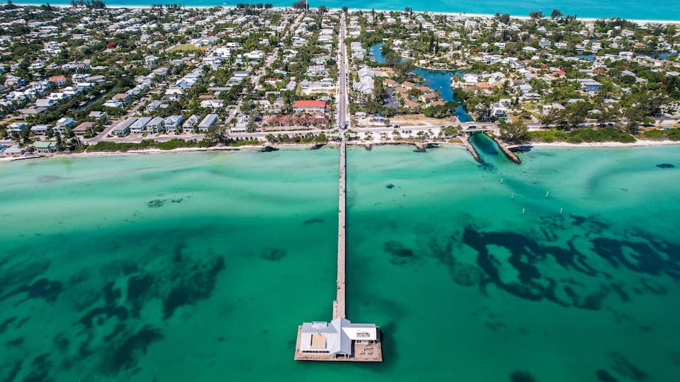 An aerial view of a coastal town with a long pier extending into turquoise waters.