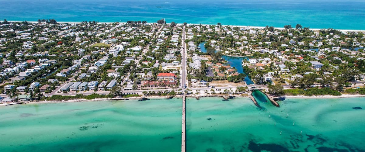 An aerial view of a coastal town with a long pier extending into turquoise waters.