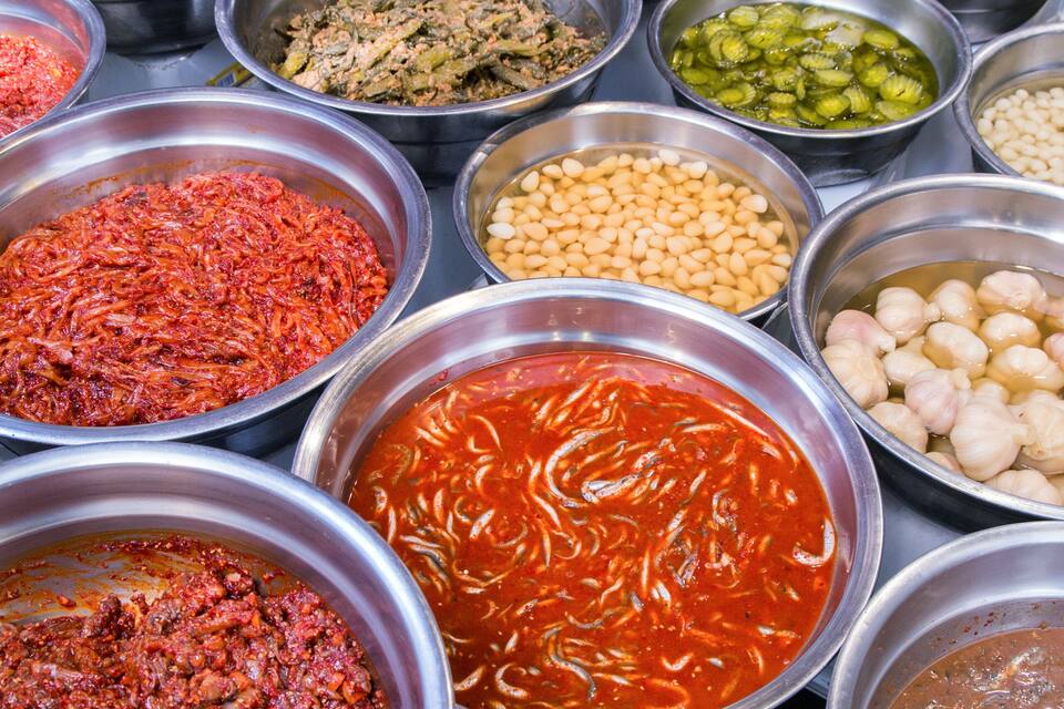 Variedad de alimentos en recipientes metálicos, como frijoles, pepinillos y diferentes salsas.