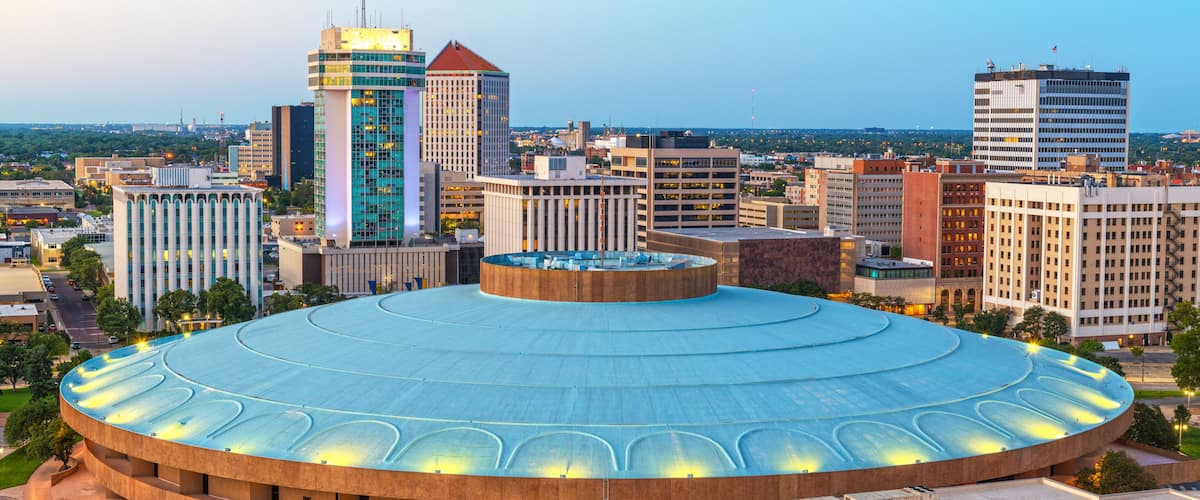 A large circular building with a blue roof surrounded by a cityscape.