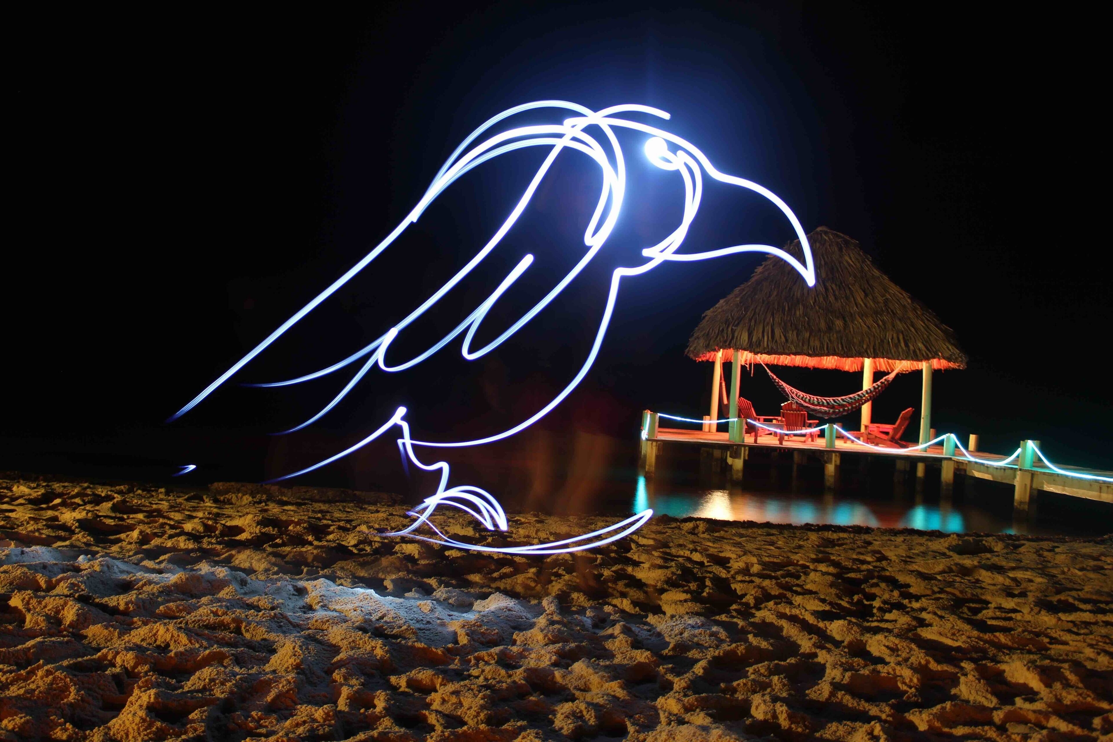 A beach at night with a thatched-roof hut and a hammock.