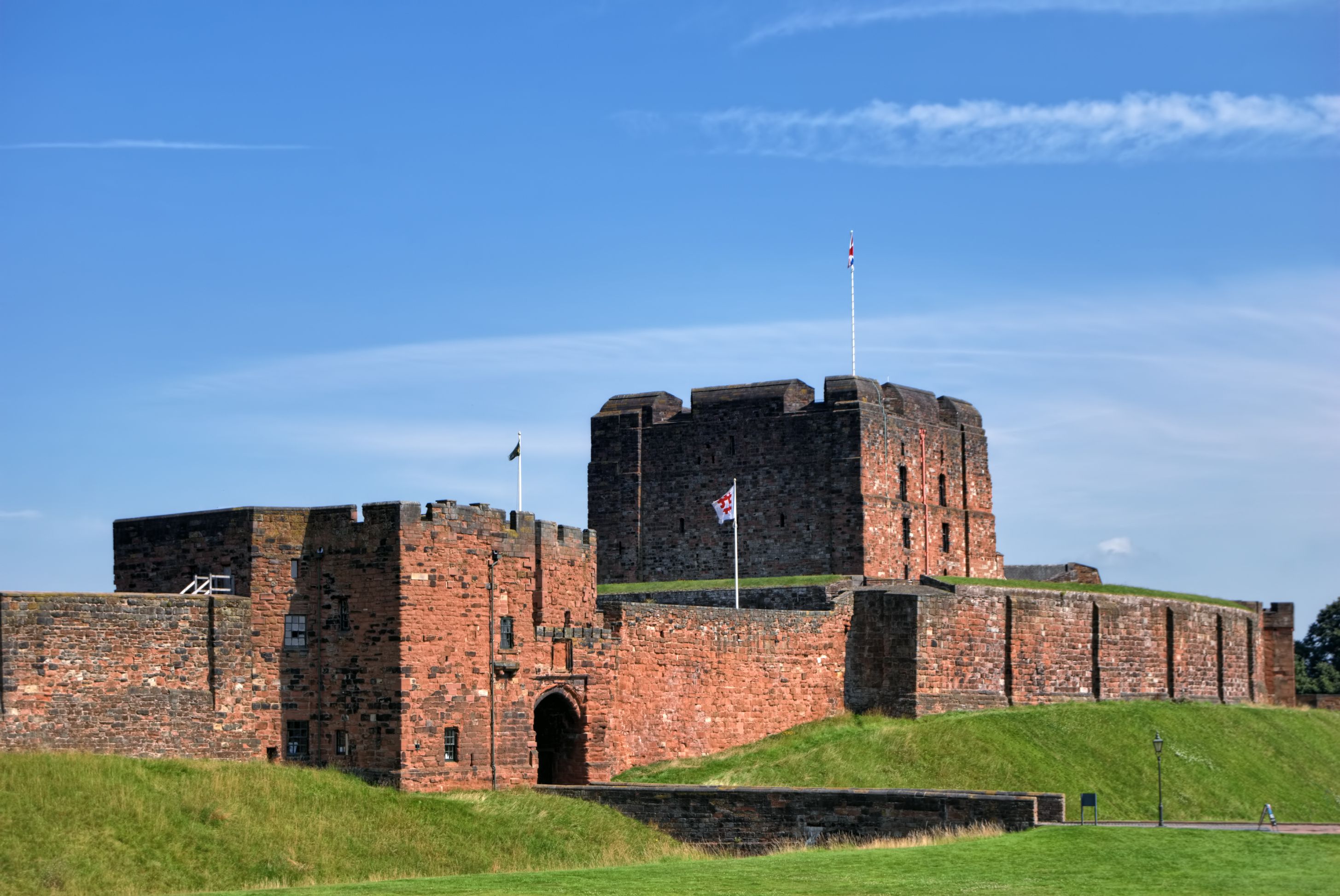 Castelo de tijolos históricos com uma bandeira no topo, com um céu azul límpido ao fundo.