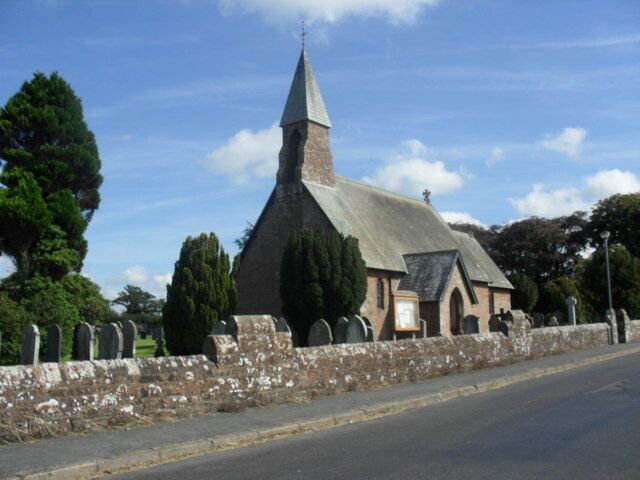 A church with a pointed steeple, surrounded by trees and a stone wall.